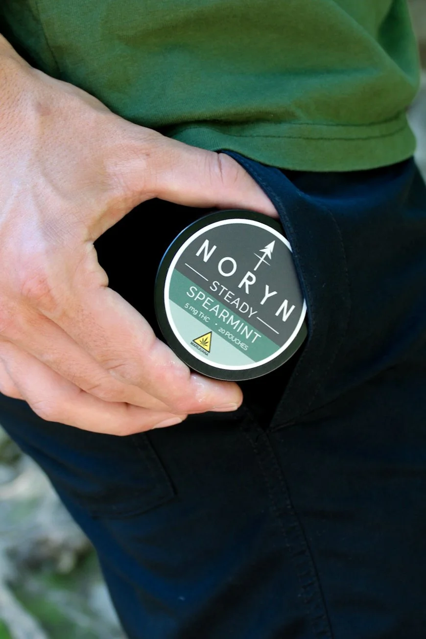 A person holding a container of NORYN Steady Spearmint cannabis product in their pocket.