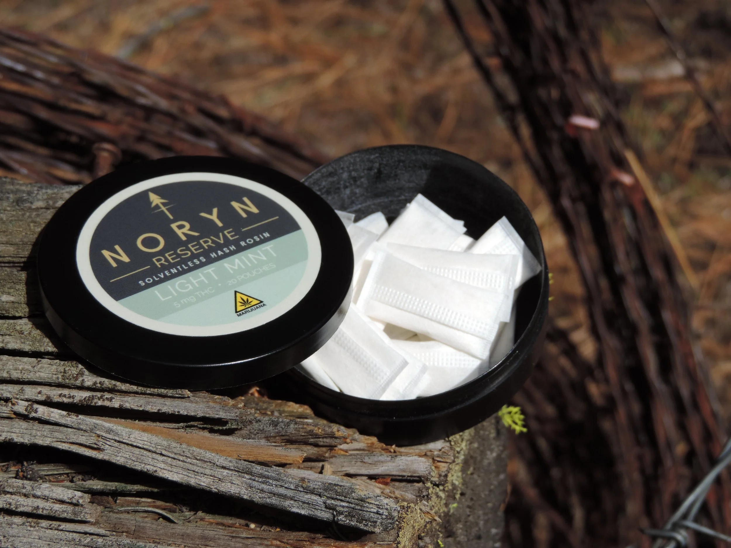 Container of THC mints labeled 'NORYN Reserve Light Mint' with white packaging inside, placed on a weathered wooden surface outdoors.