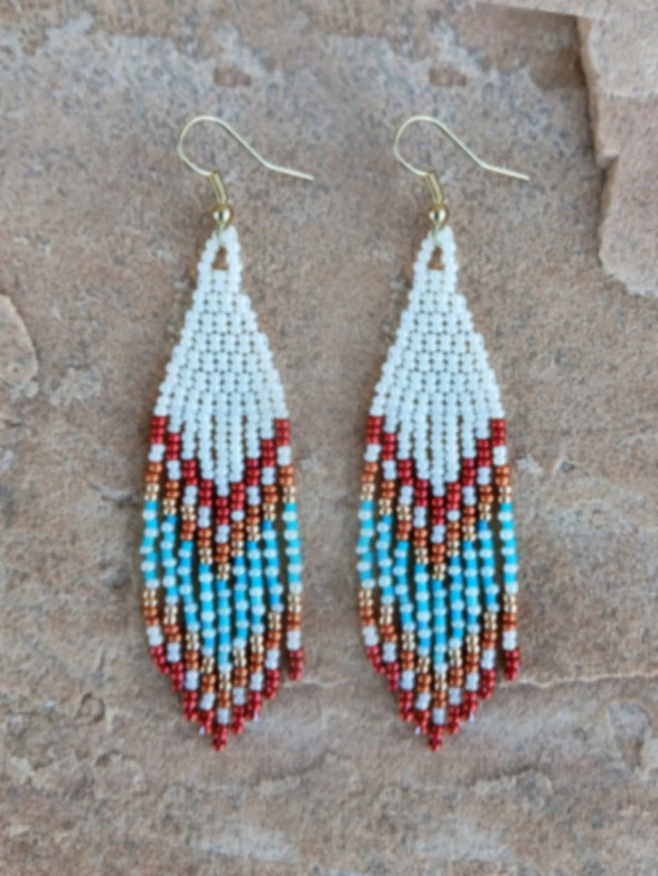 Handmade Southwestern beaded fringe dangle earrings handwoven in an ivory white, red, gold, orange, and blue desert sunset color palette.