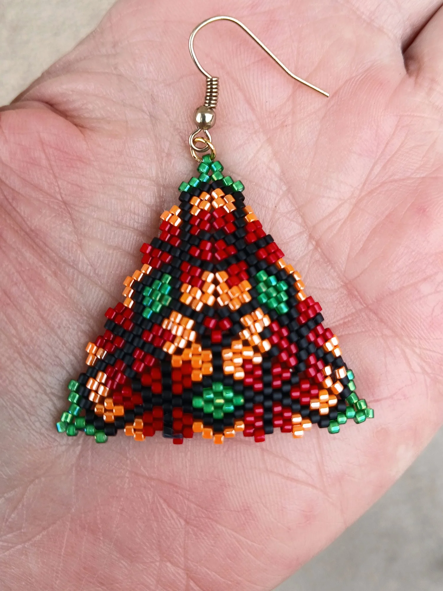 Handmade geometric triangle beaded earrings featuring a colorful floral pattern handwoven in red, green, orange, and black peyote stitch.