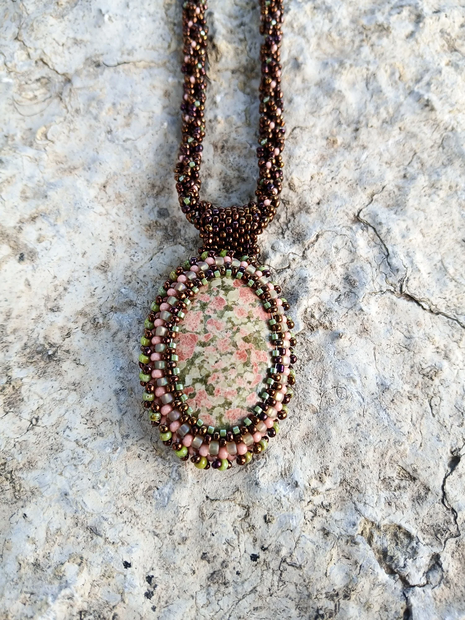 Handmade pendant necklace featuring a polished, beaded bezeled Unakite gemstone with intricate beadwork on a matching chain