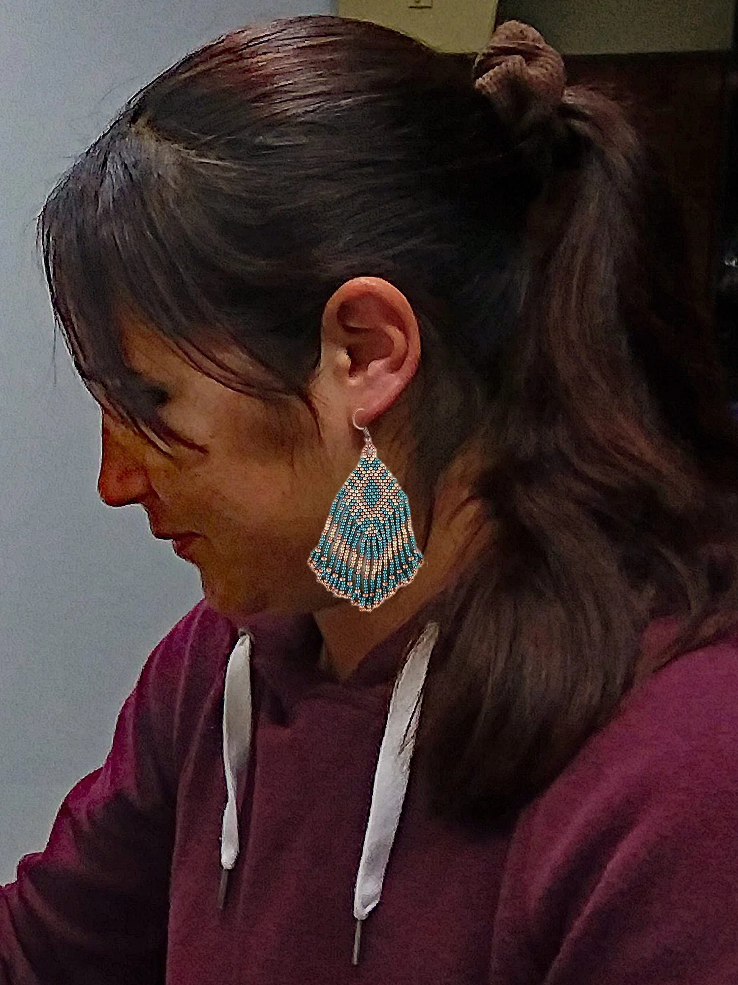 Model wearing Handmade Southwestern beaded fringe dangle earrings handwoven in an earthy green, metallic gold, and copper color palette.