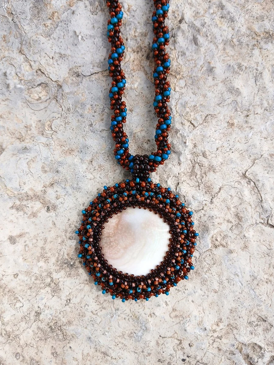 Handmade nature-inspired beaded necklace featuring a beaded bezel on natural spiral Shiva snail shell pendant handwoven in blue, and brown seed beads.
