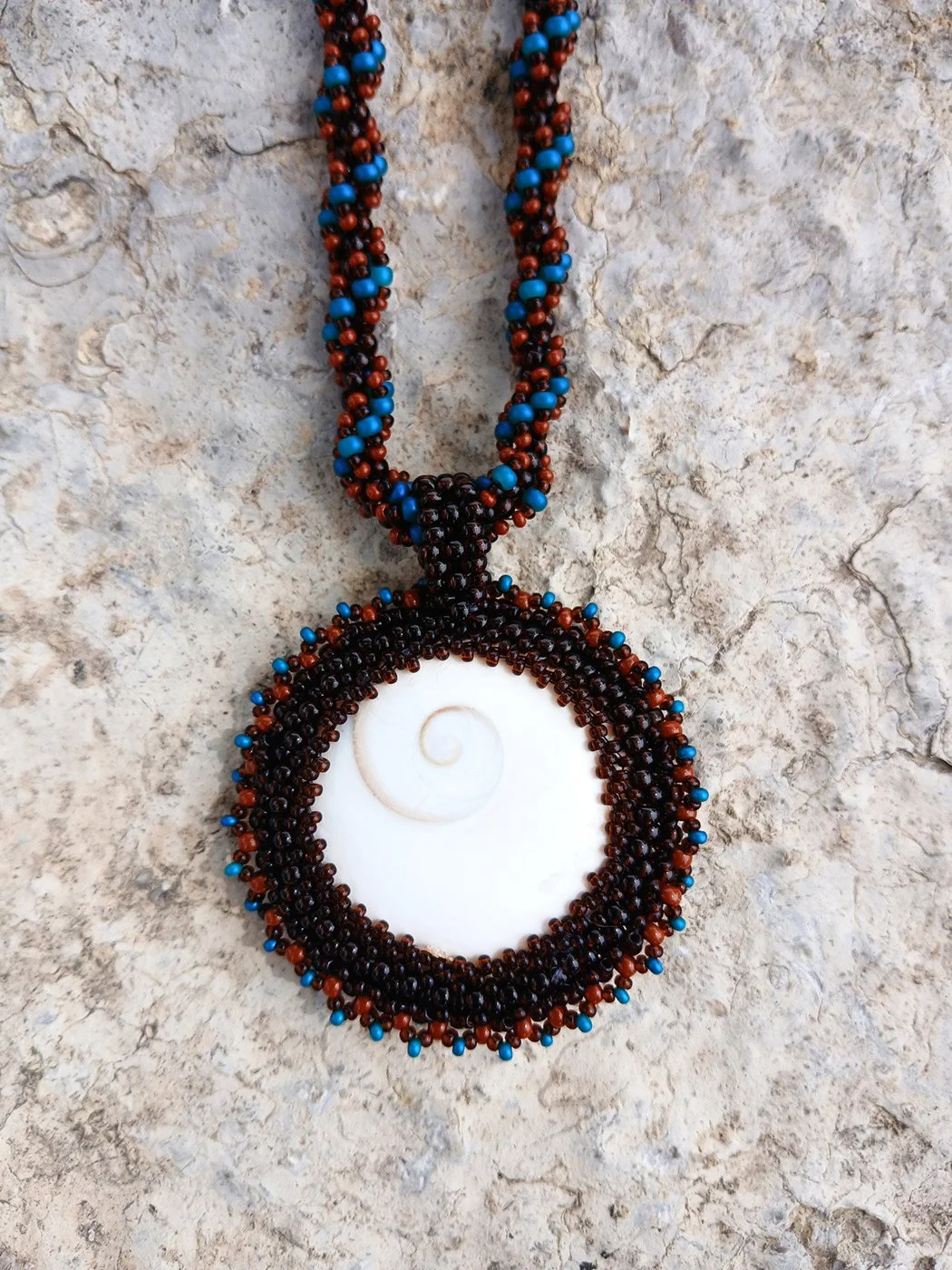 Handmade nature-inspired beaded necklace featuring a beaded bezel on natural spiral Shiva snail shell pendant handwoven in blue, and brown seed beads.