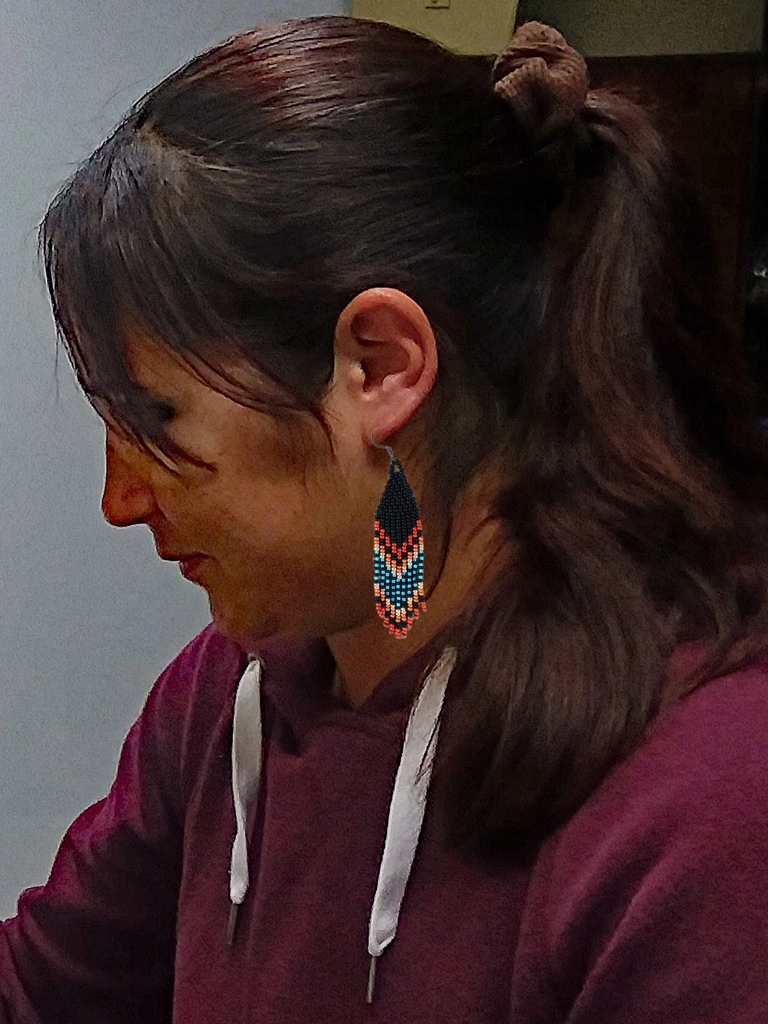 Handmade Southwestern beaded fringe dangle earrings handwoven in a rich black, red, blue, gold, and copper mountain sunset color palette on model.