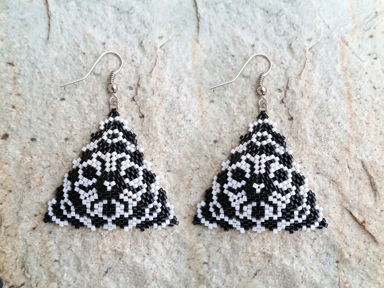 Handmade geometric triangle beaded earrings featuring an abstract lion face design handwoven in black and white peyote.