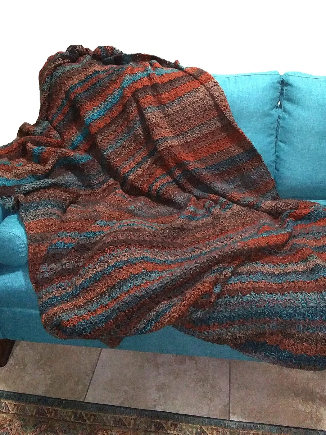 An oversized, colorful Painted Desert thick crochet blanket in rust, brown, and teal tones.