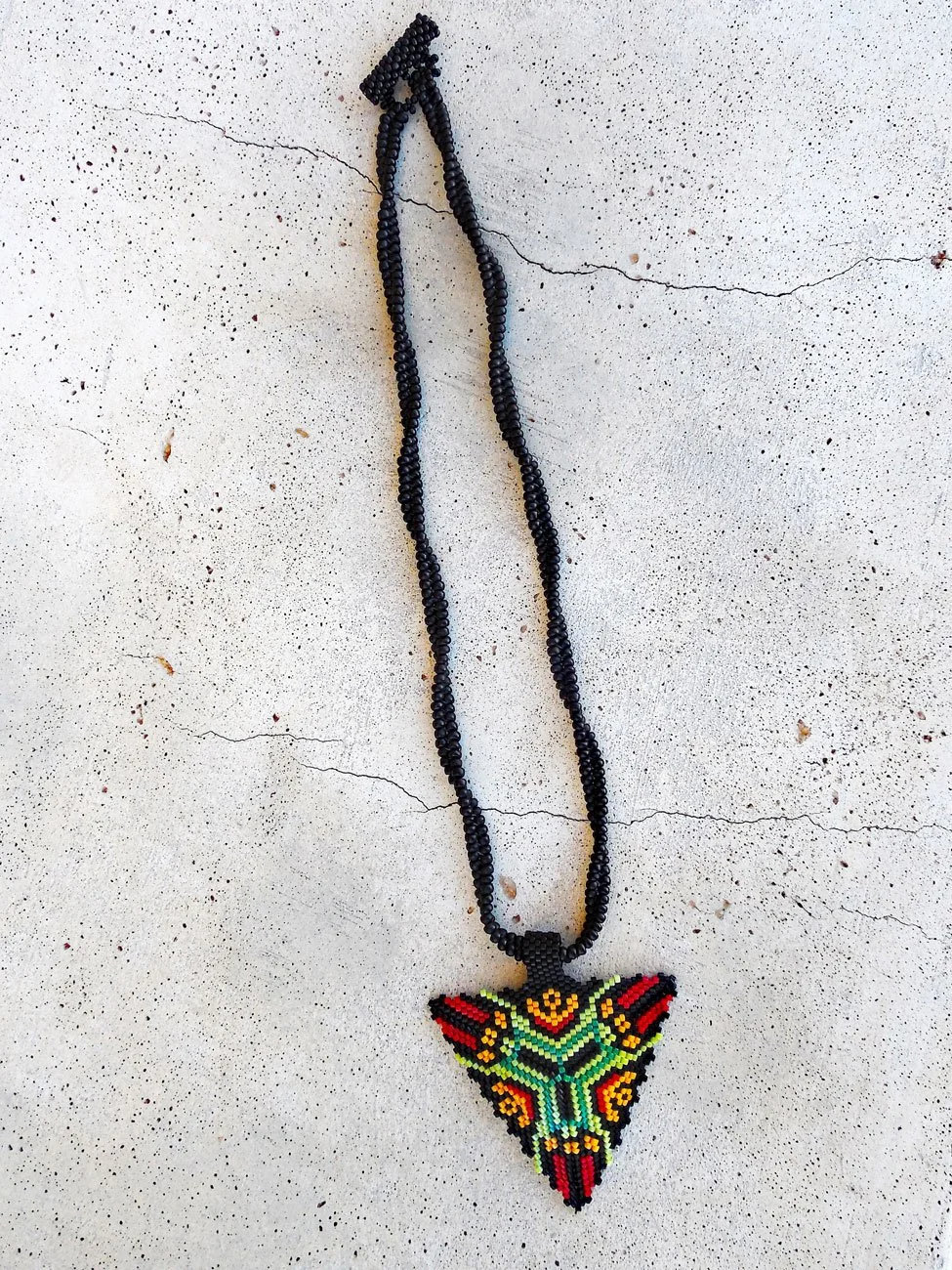 Handmade geometric triangle pendant necklace featuring handwoven herringbone and peyote stitch nonmetal beaded chain in black, green, yellow, and red.