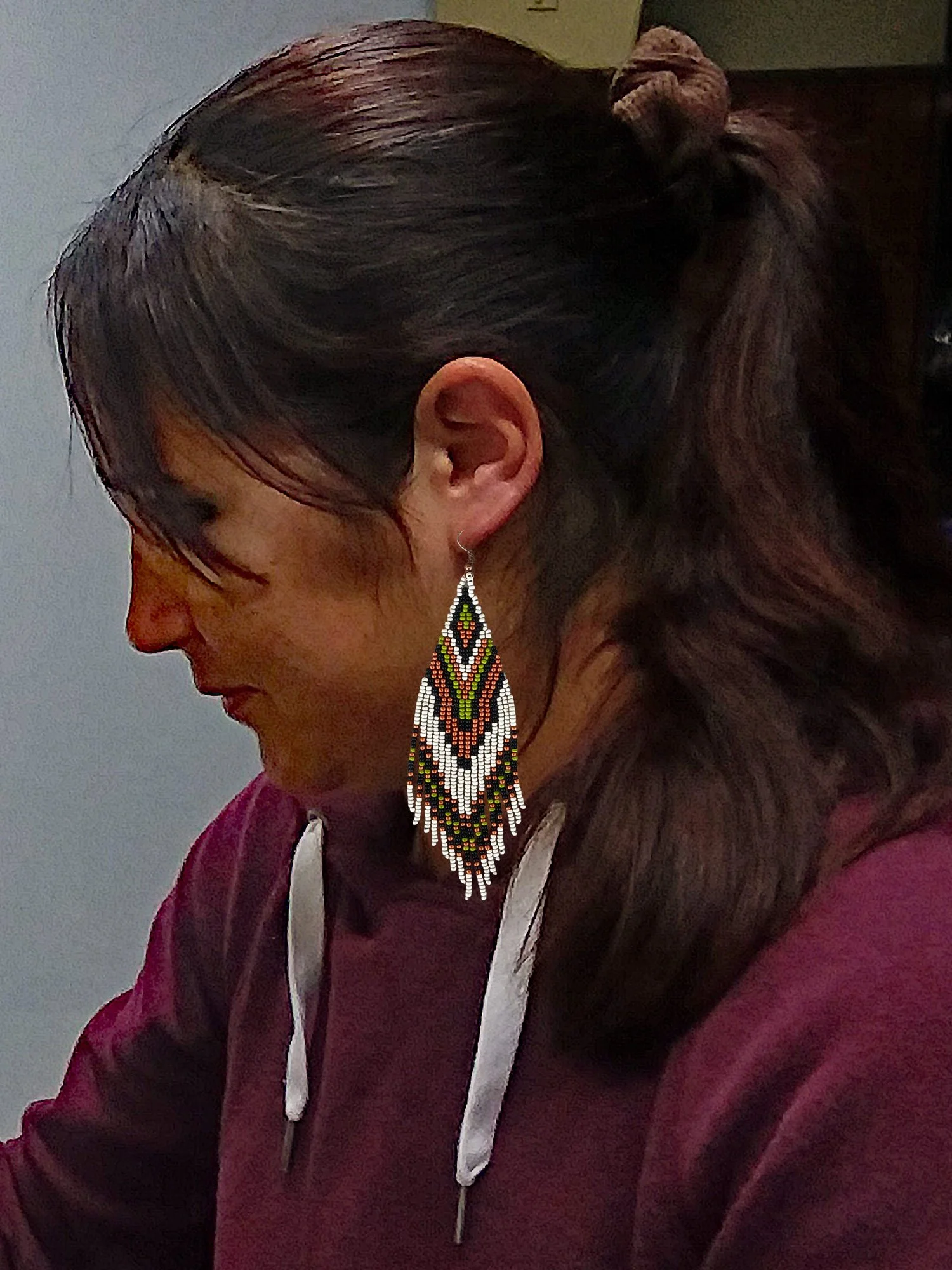 Handmade 5” beaded fringe earrings handwoven in chevron brick stitch with green, matte silver, black, and copper on model.