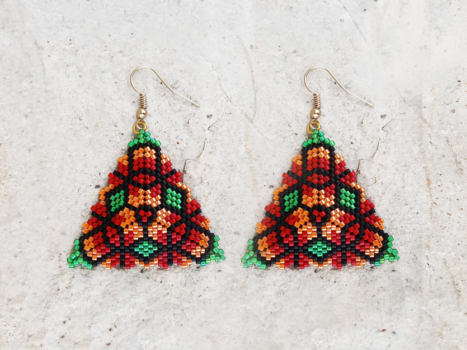 Handmade geometric triangle beaded earrings featuring a colorful floral pattern handwoven in red, green, orange, and black peyote stitch.