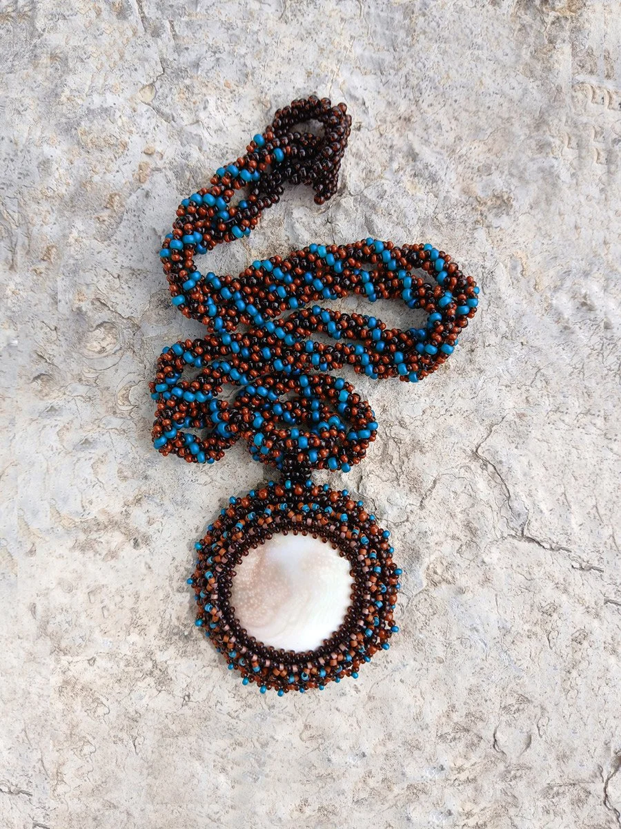 Handmade nature-inspired beaded necklace featuring a beaded bezel on natural spiral Shiva snail shell pendant handwoven in blue, and brown seed beads.
