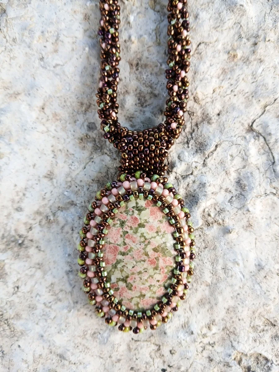 Handmade statement pendant necklace featuring a natural olive green and pink unakite gemstone cabochon handwoven with a matching bronze beaded chain.