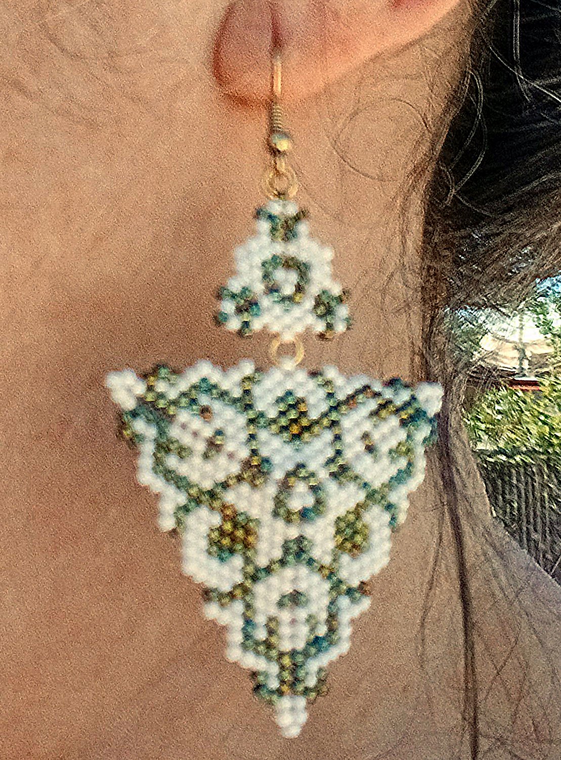 Handmade green and alabaster white geometric triangle drops with two triangles beaded earrings in handwoven in peyote stitch design on model.