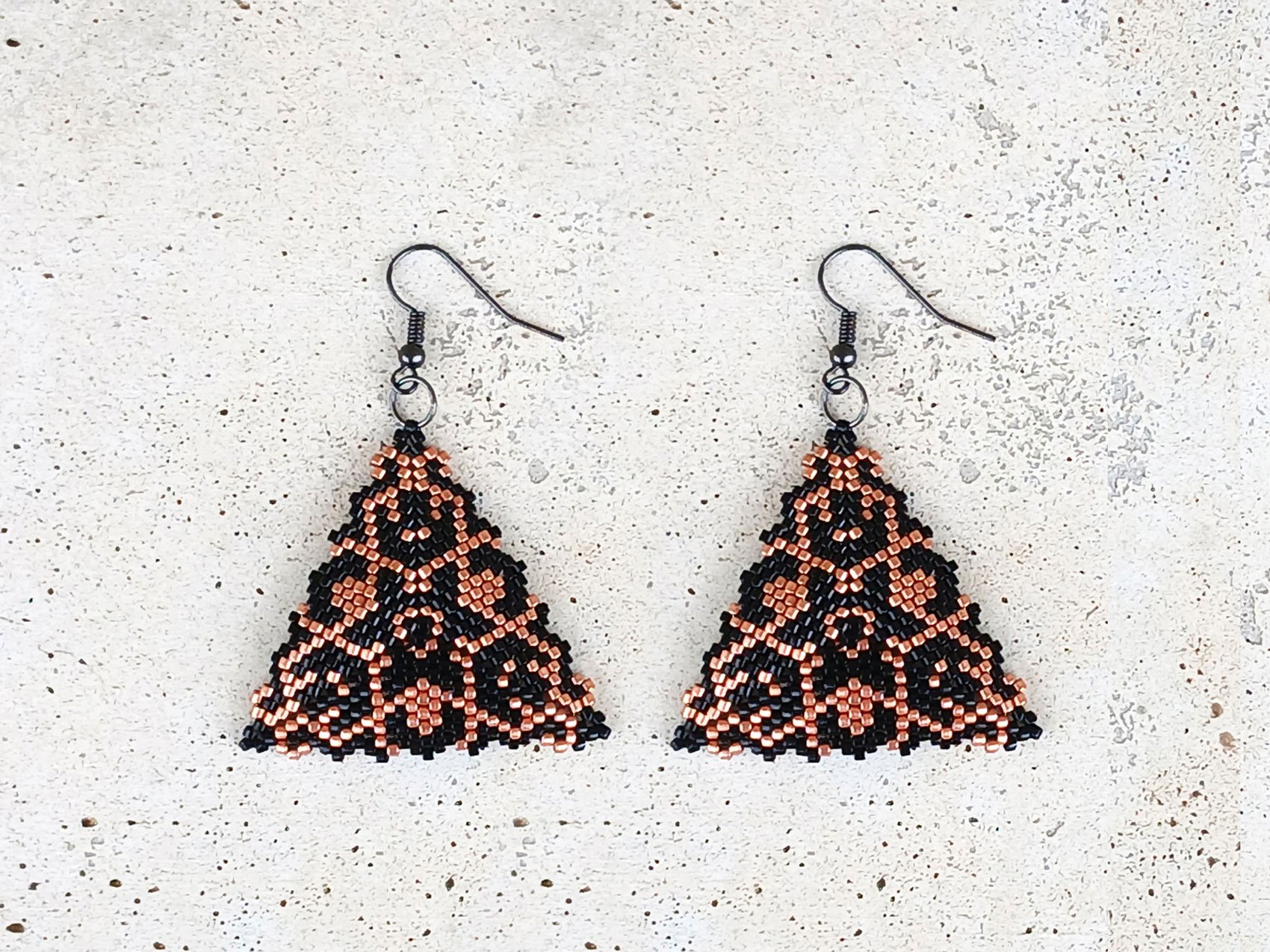 Handmade geometric triangle beaded dangle earrings featuring a handwoven black and copper peyote-stitch star center design.