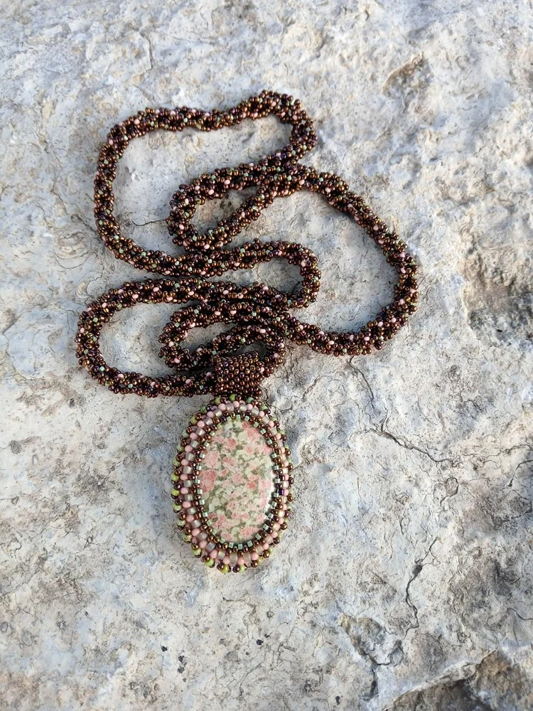 Handmade statement pendant necklace featuring a natural olive green and pink unakite gemstone cabochon handwoven with a matching bronze beaded chain.