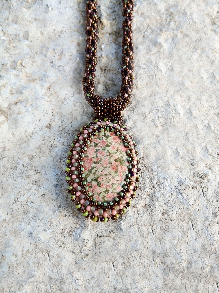 Handmade statement pendant necklace featuring a natural olive green and pink unakite gemstone cabochon handwoven with a matching bronze beaded chain.