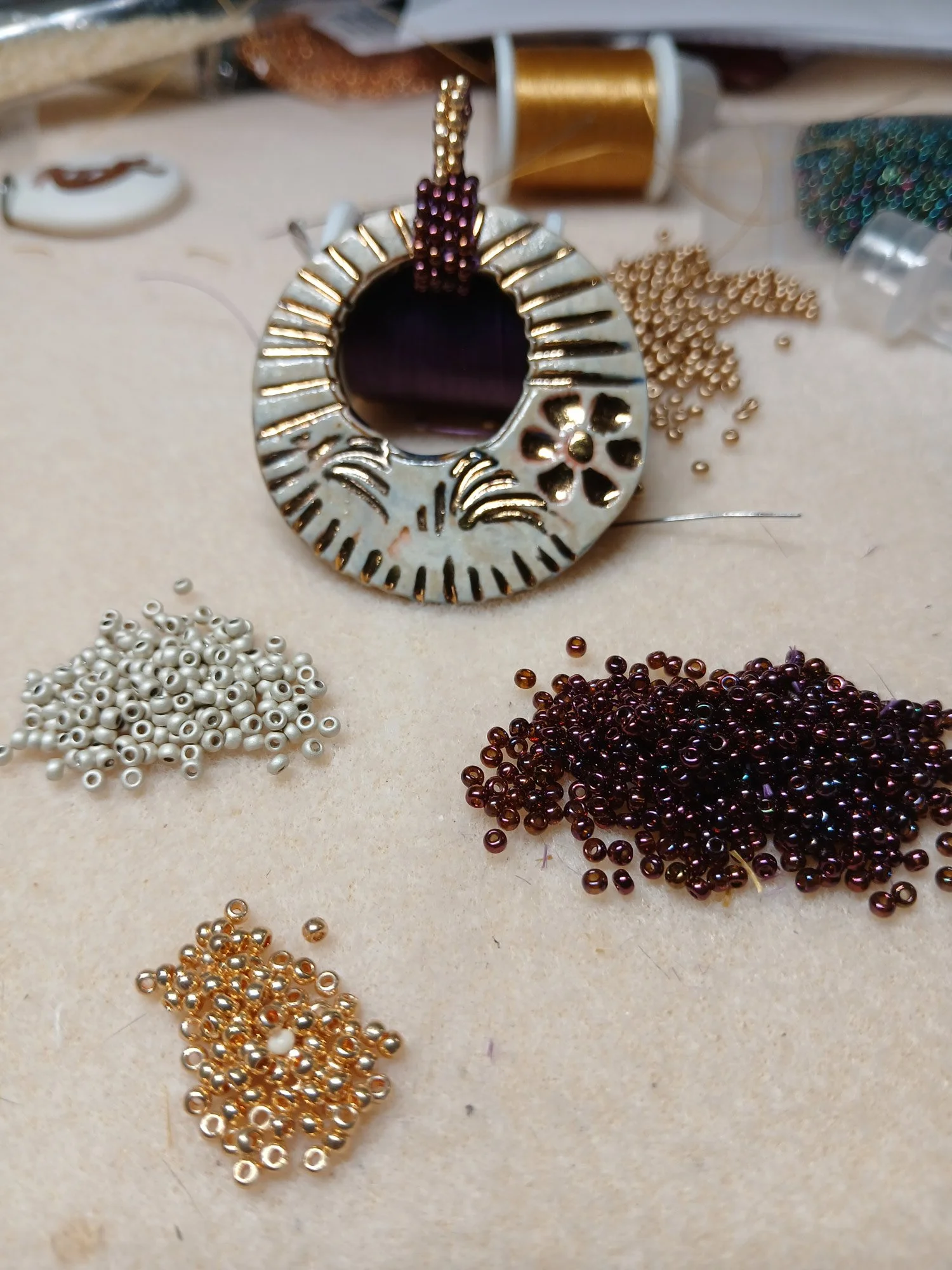 Artisan workbench showing an initial handmade beaded bail design layout for a ceramic pendant necklace.