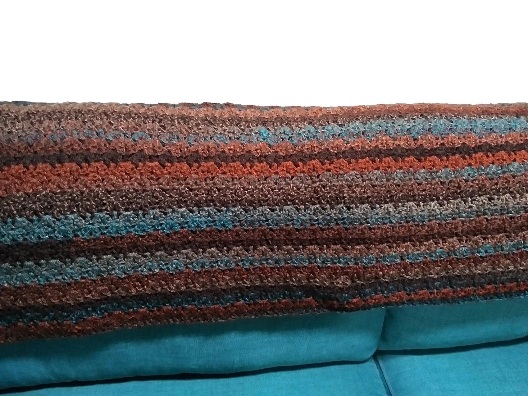 An oversized, colorful Painted Desert thick crochet blanket in rust, brown, and teal tones.
