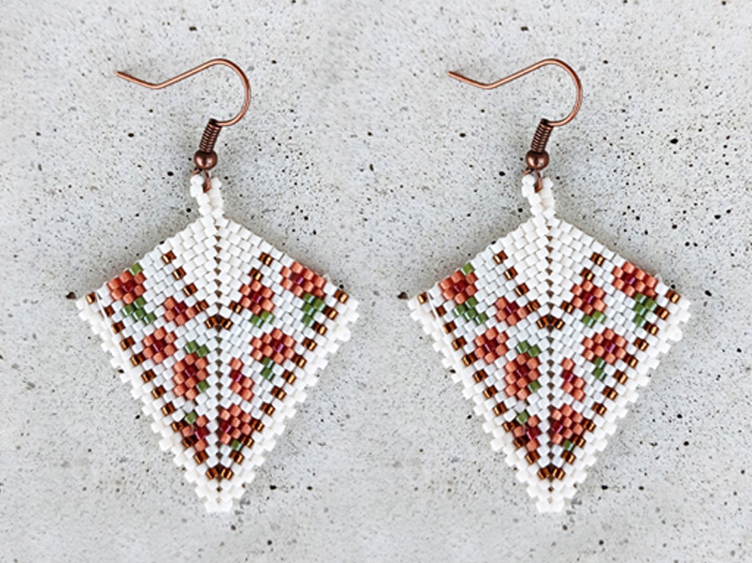Elegant handmade geometric kite drop beaded earrings handwoven with a soft ivory and peach floral pattern and shimmering metallic gold accents.