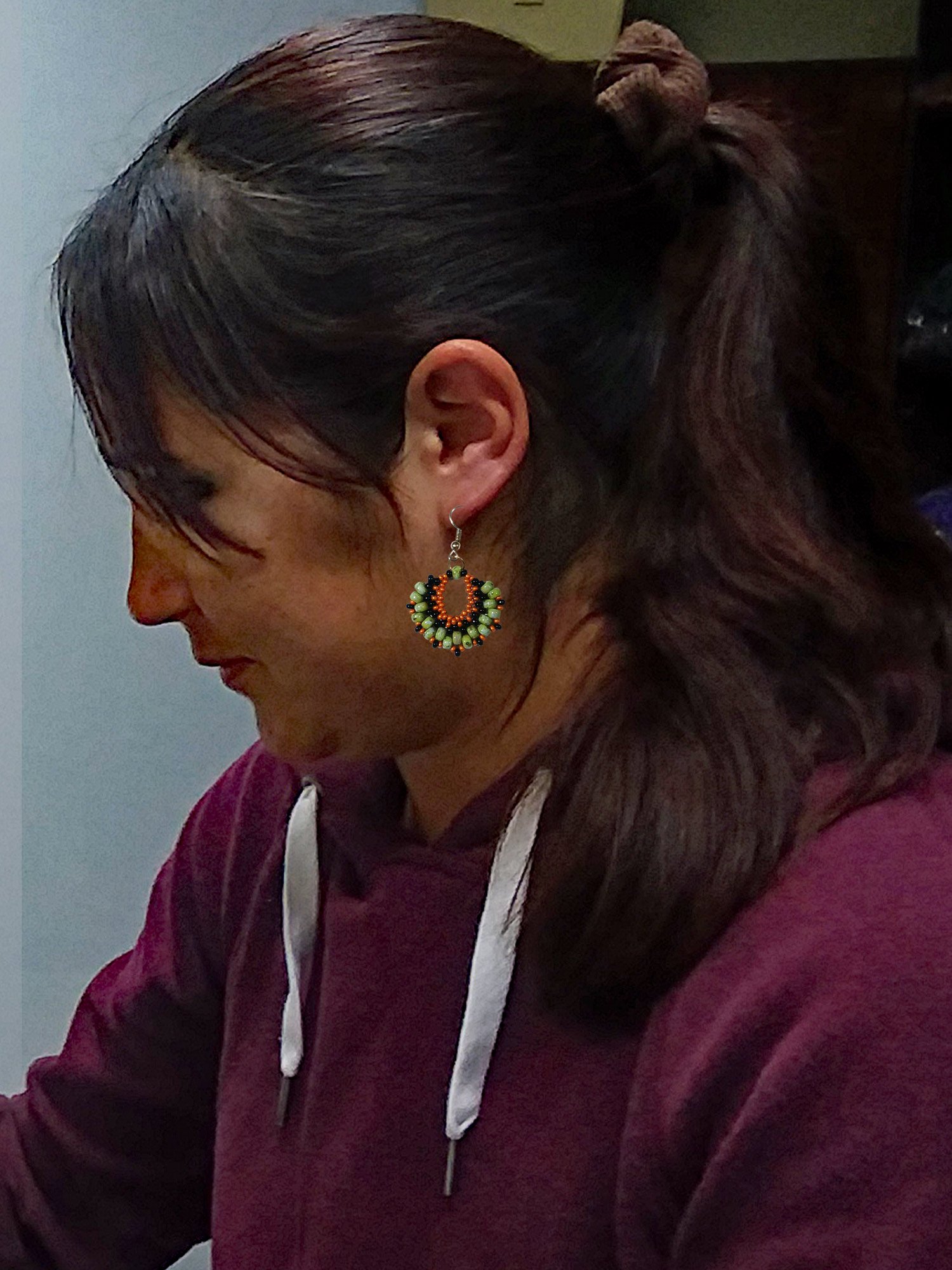 Model wearing handmade beaded crescent fan short dangle earrings handwoven in Picasso green, orange, and black glass seed beads.