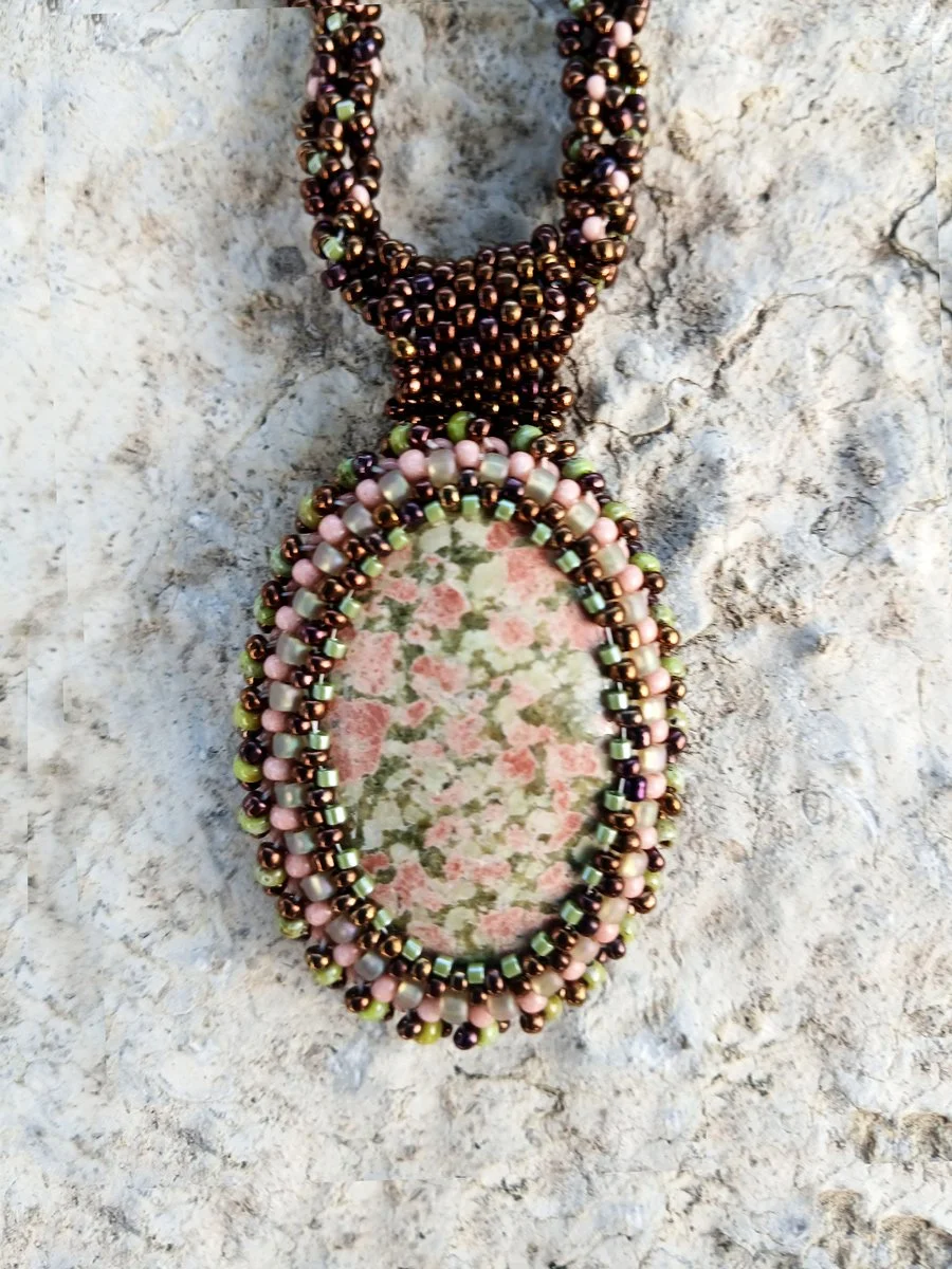 Handmade statement pendant necklace featuring a natural olive green and pink unakite gemstone cabochon handwoven with a matching bronze beaded chain.