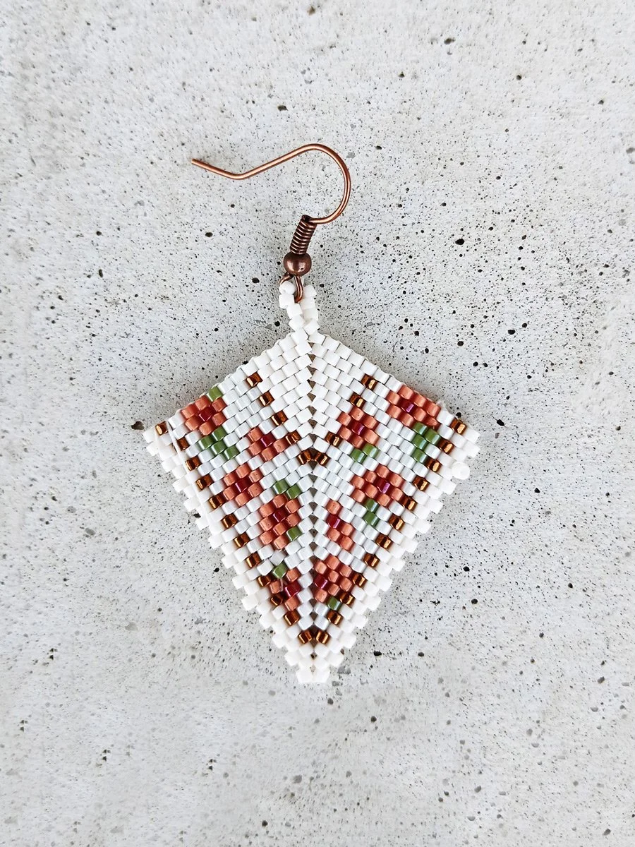 Elegant handmade geometric kite drop beaded earrings handwoven with a soft ivory and peach floral pattern and shimmering metallic gold accents.