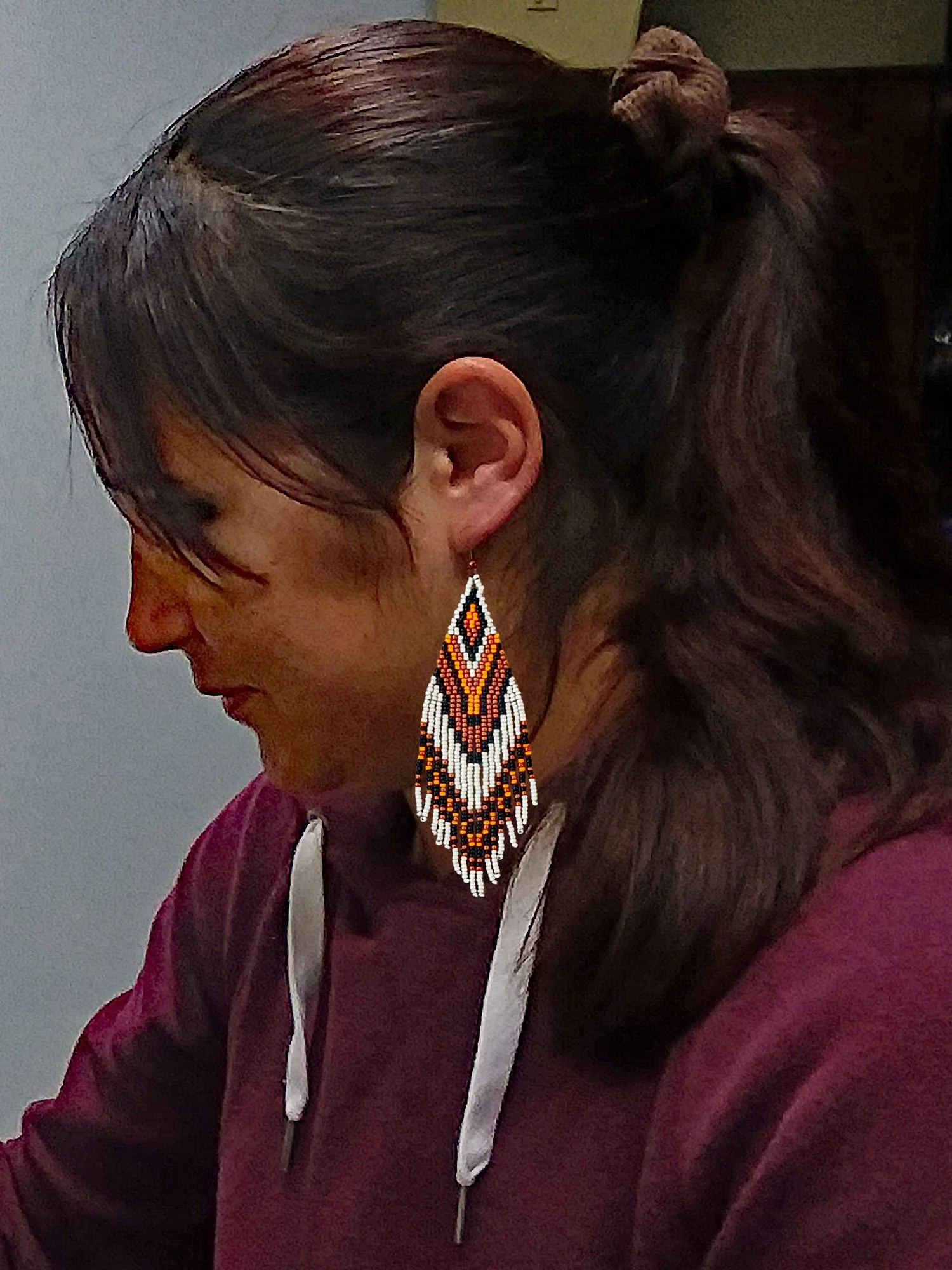 Handmade 5" sunset orange and black beaded fringe earrings handwoven with accents of rich copper, and matte silver beads on model.