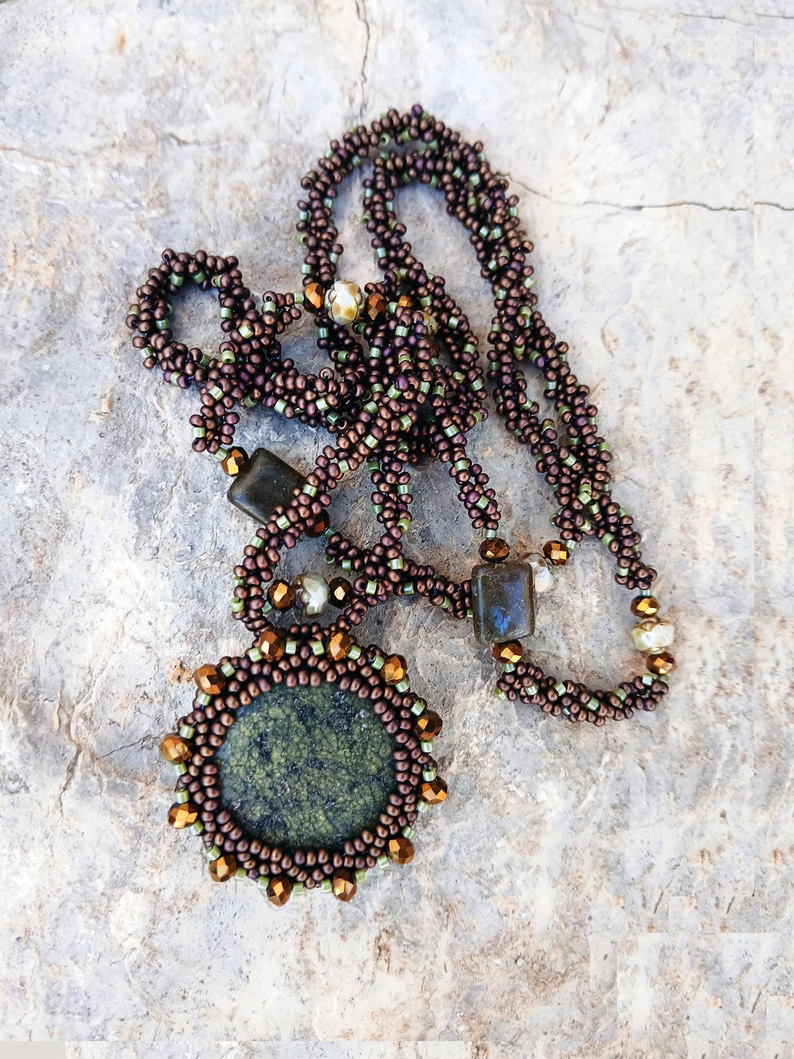 Handmade statement pendant necklace featuring a natural forest green agate gemstone wrapped in handwoven beaded bezel with a brown and bronze chain.