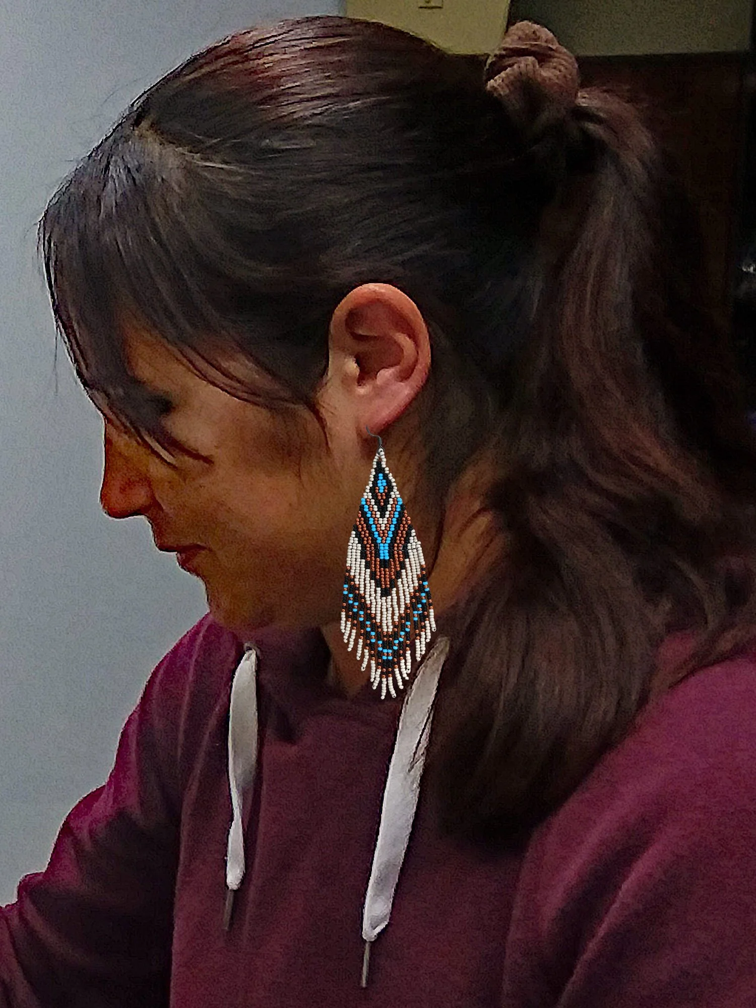 Handmade 5” beaded fringe earrings handwoven in chevron brick stitch with sky blue, matte silver, black, and copper on model.