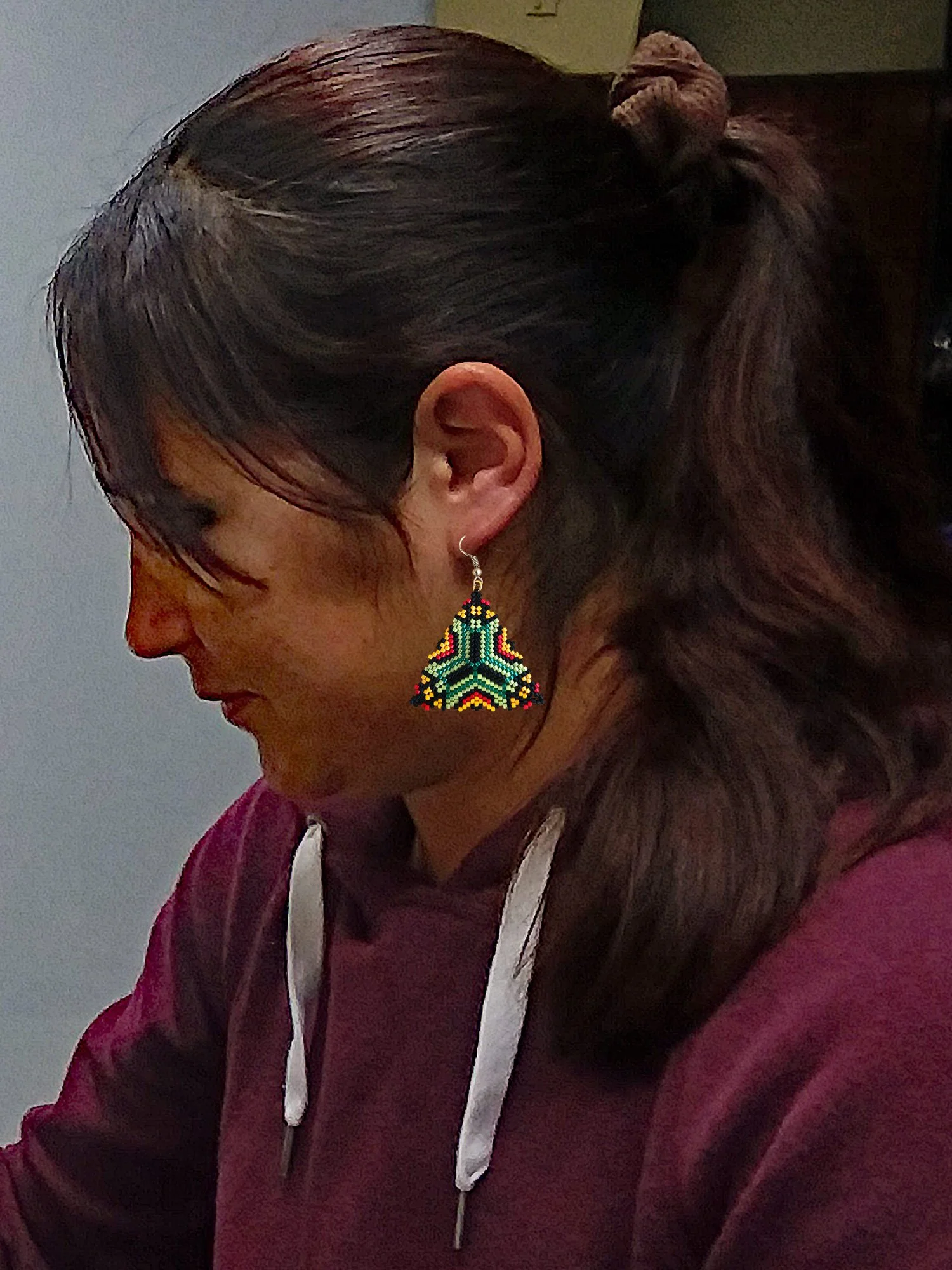 Handmade southwestern geometric triangle peyote beaded dangle earrings featuring a handwoven in green, red, black, and orange color palette on model.