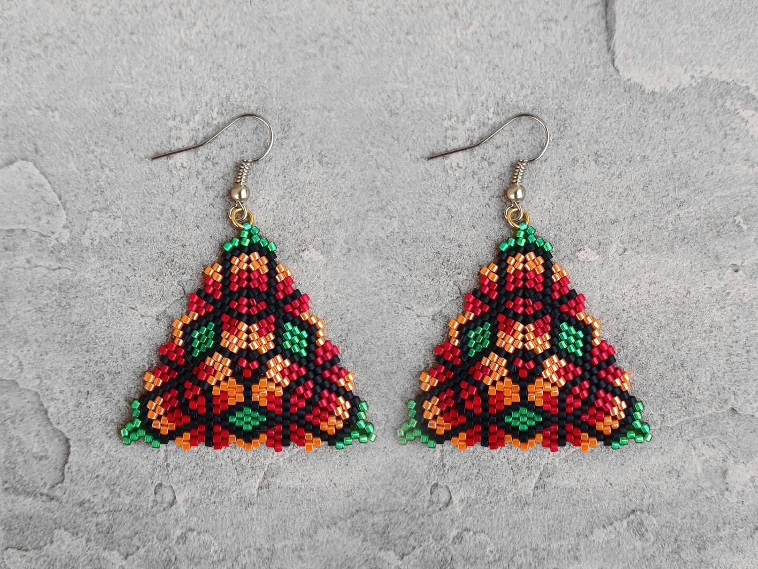 Handmade geometric triangle beaded earrings featuring a colorful floral pattern handwoven in red, green, orange, and black peyote stitch.