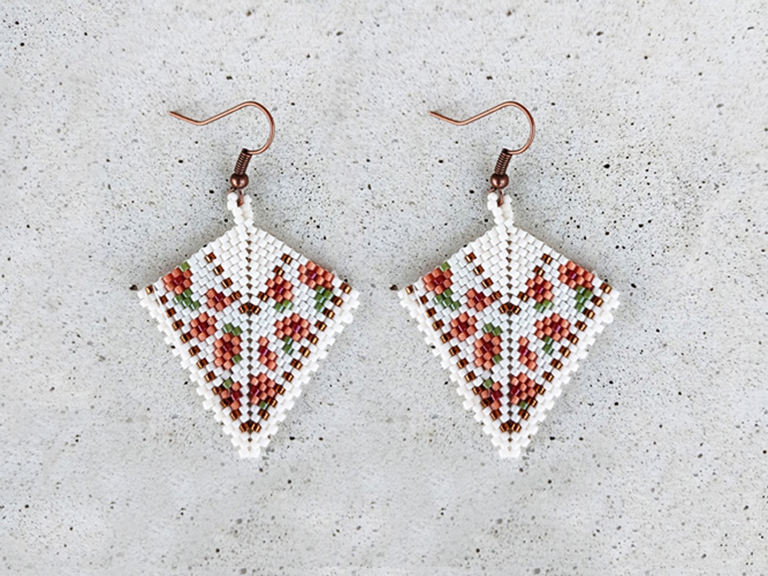 Elegant handmade geometric kite drop beaded earrings handwoven with a soft ivory and peach floral pattern and shimmering metallic gold accents.