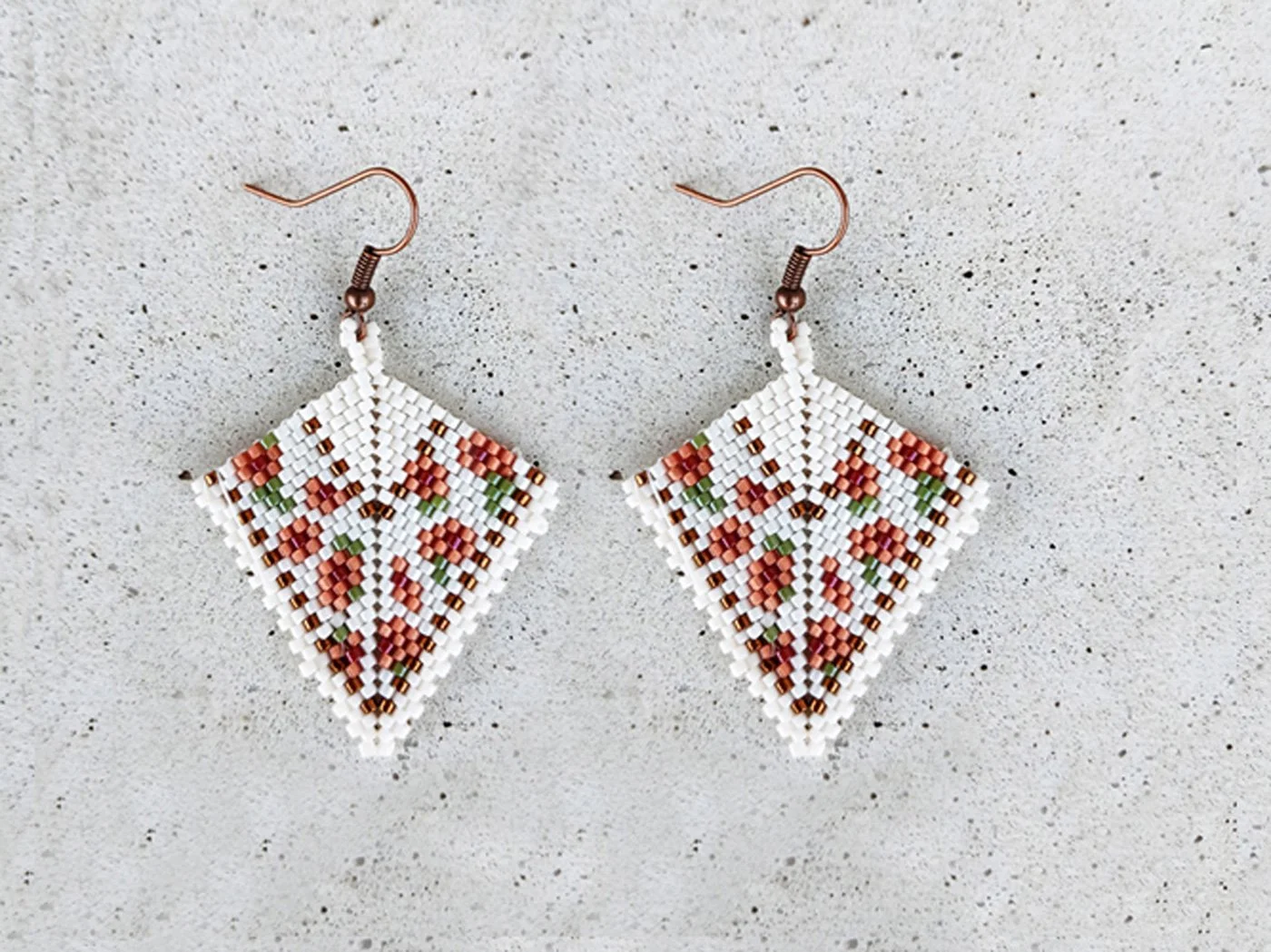 Elegant handmade geometric kite drop beaded earrings handwoven with a soft ivory and peach floral pattern and shimmering metallic gold accents.