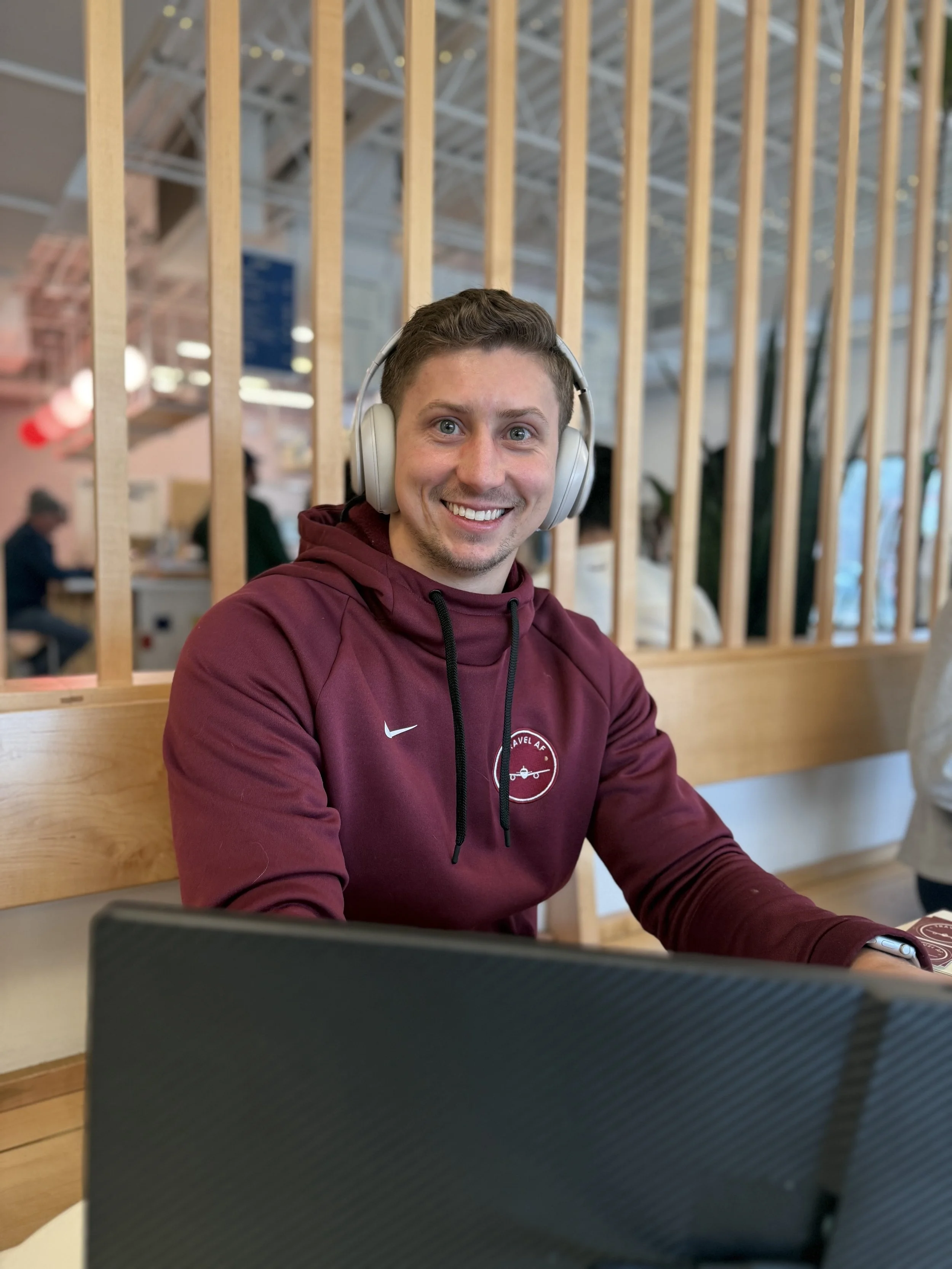 Austin Riffe, points strategist and founder of Travel AF, wearing a maroon Travel AF hoodie and headphones at a coffee shop