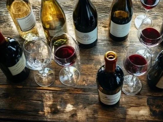 Several bottles of wine and filled wine glasses on a rustic wooden table.