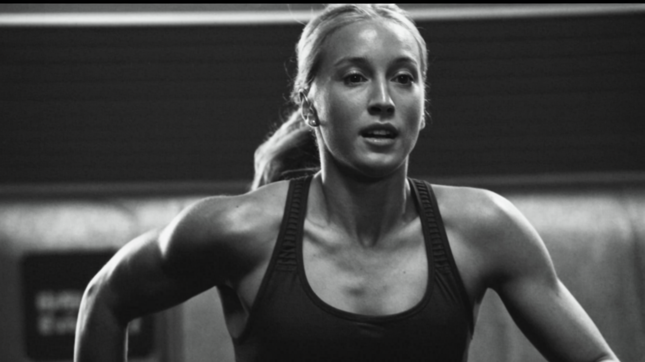 Een zwart-wit foto van een jonge vrouw die aan het hardlopen is, met een sporttop en een gefronste blik.