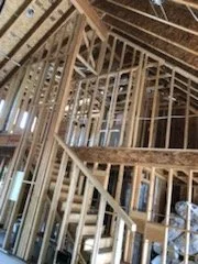 Interior of a building under construction with exposed wooden framing and roof trusses.