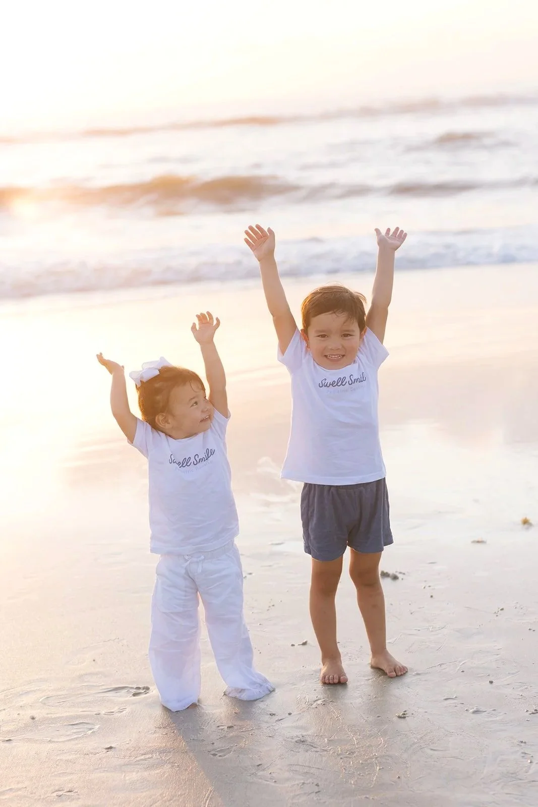 Dr. Noah Andone's two young children wearing Swell Smiles Pediatric Dentistry t-shirts on a Jacksonville beach at sunset