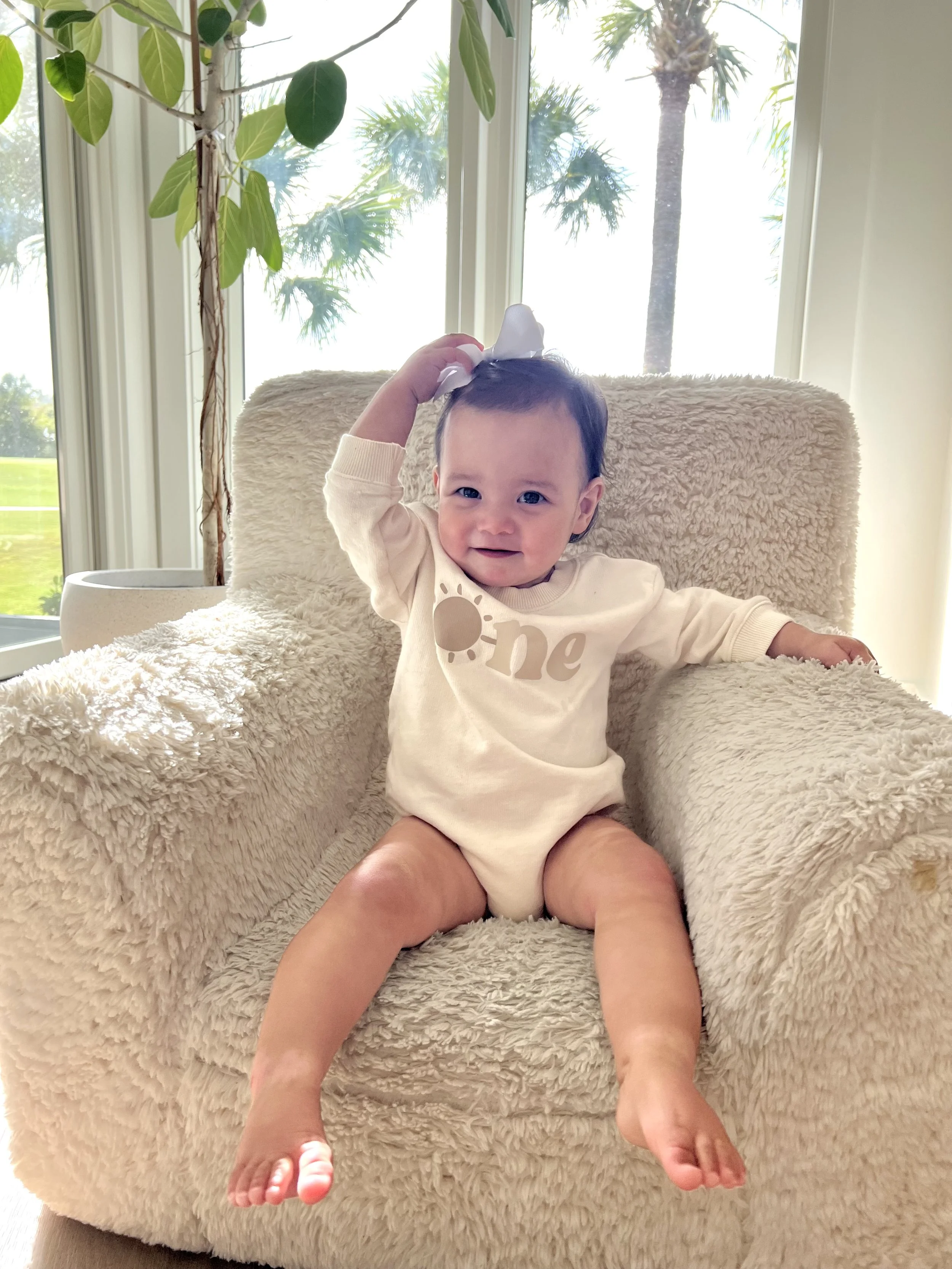 Smiling baby in a first birthday onesie, illustrating the First Tooth, First Birthday, First Visit guideline at Swell Smiles Pediatric Dentistry