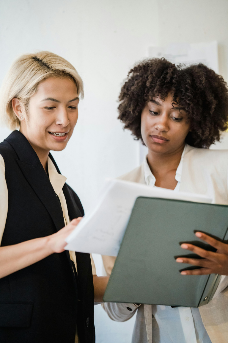Two women looking at documents and a tablet together in an office setting.