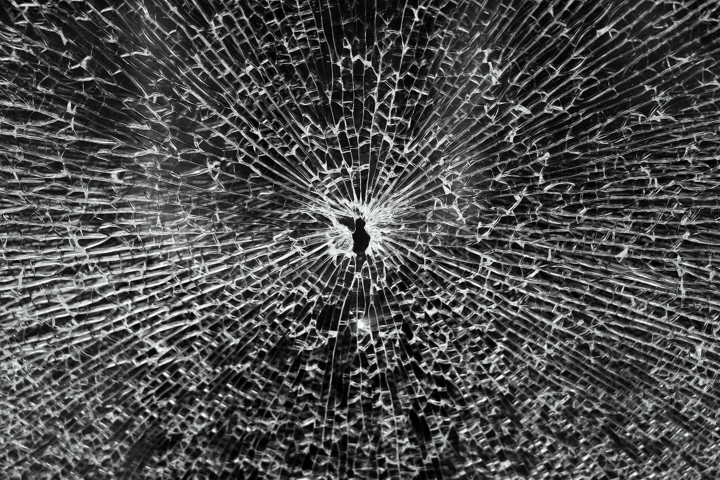 Close-up of a broken glass surface showing a spider-web pattern of shattered cracks.
