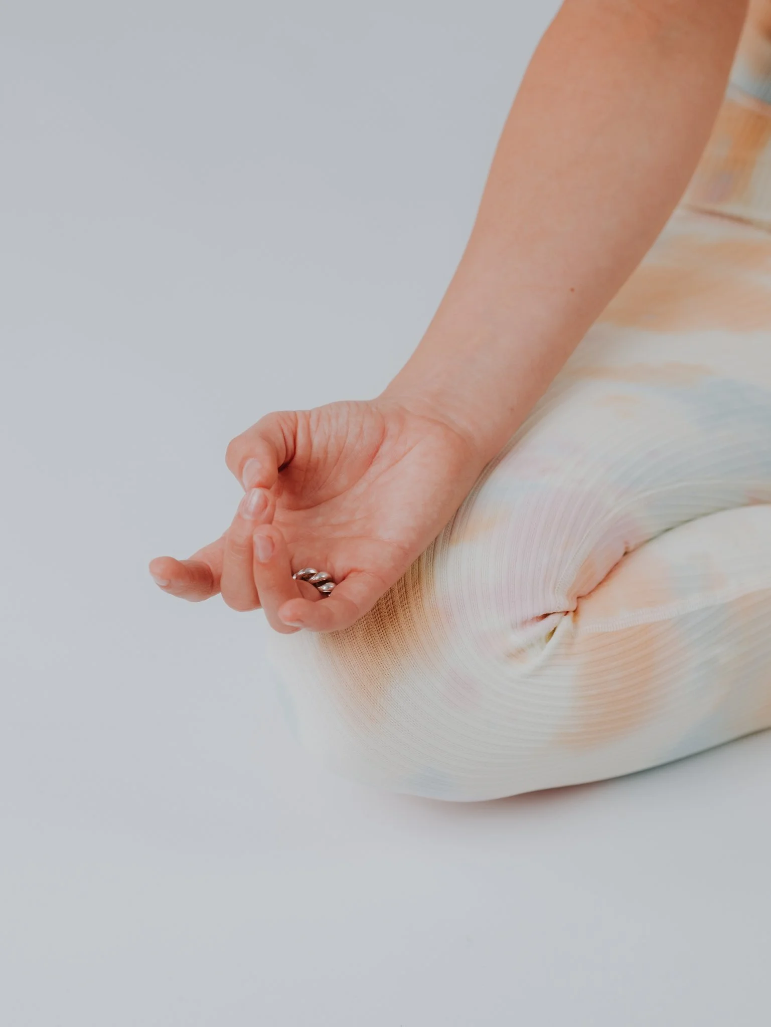 Nahaufnahme einer Hand, die Finger in Lotusposition, mit einer beige Hose und einem hellen Hintergrund.