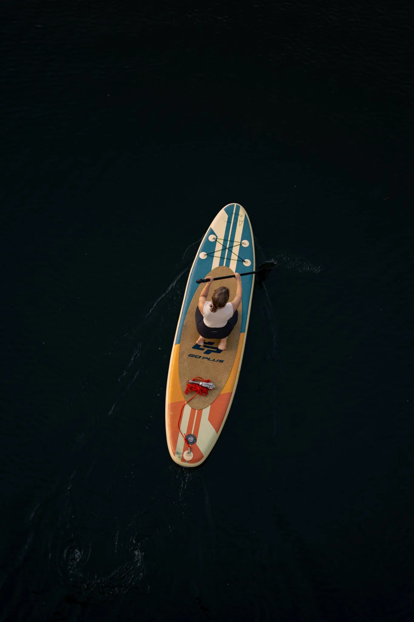 Ein Mensch auf einem Stand-up-Paddle-Board auf dunklem Wasser, vom Himmel fotografiert.