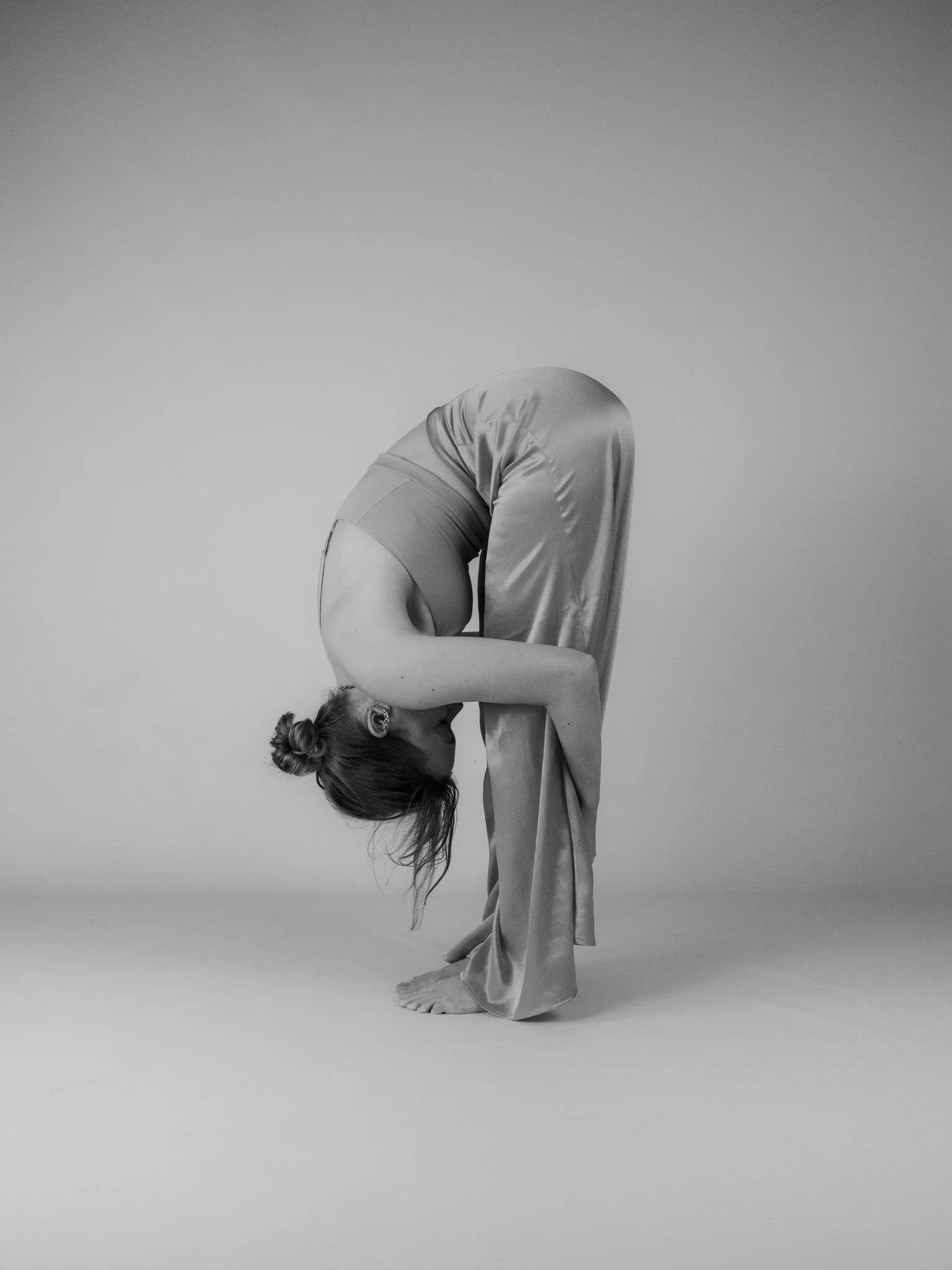 Schwarz-weiß-Foto eines Menschen in sportlicher Kleidung, der in einer Yoga-Pose steht, die den Körper in einer bent-over Position zeigt, mit der Kopf nach unten und den Armen auf dem Boden.
