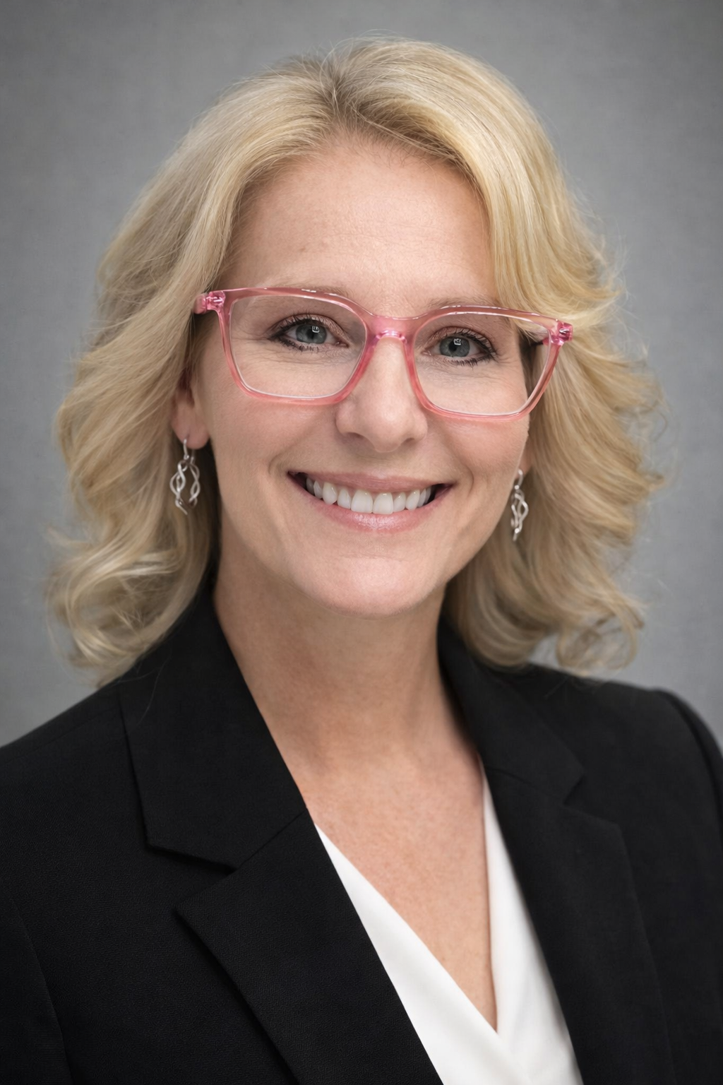 A woman with blonde hair, pink glasses, and earrings smiling in a professional portrait.
