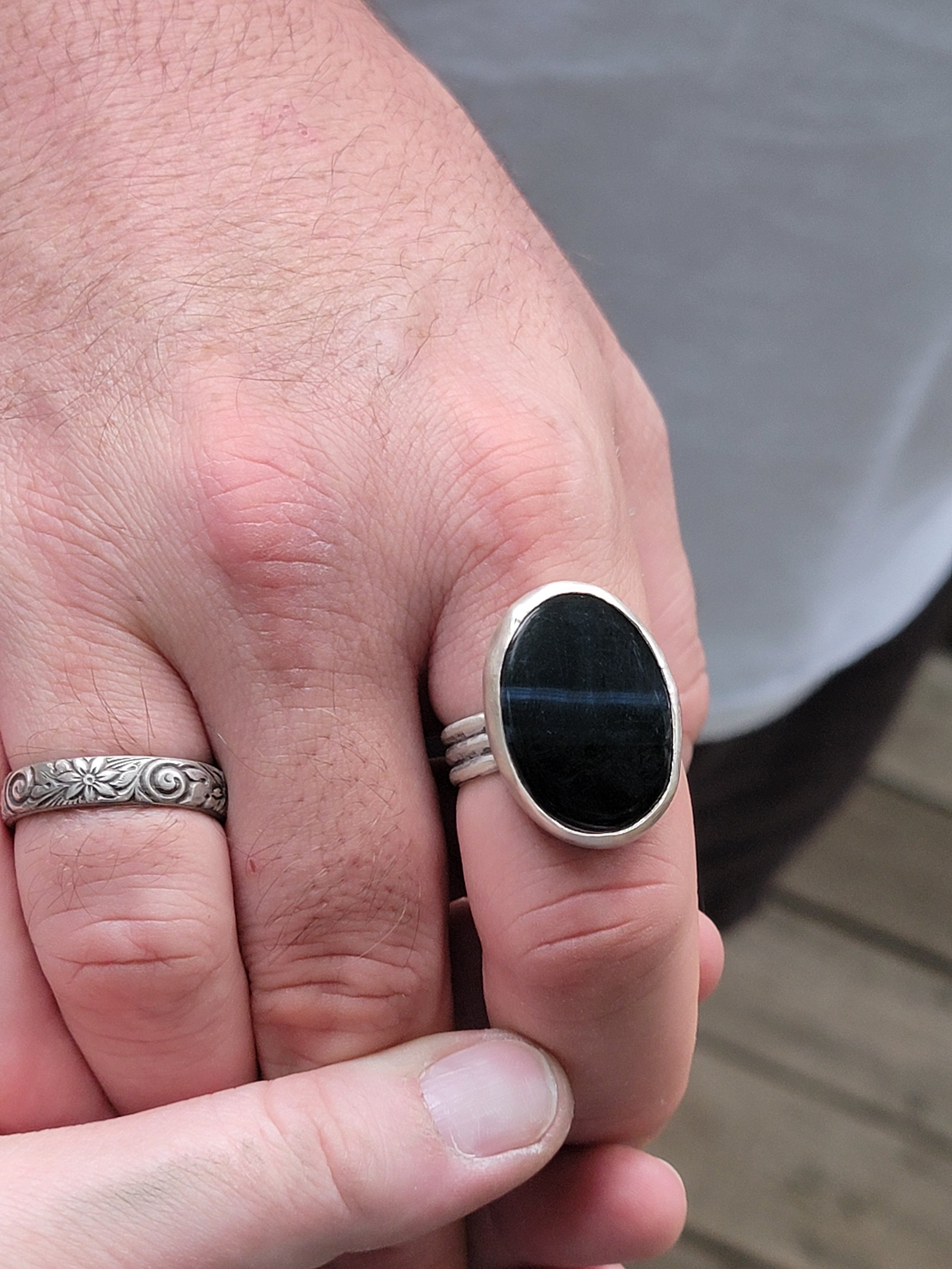 Close-up of a person's hand wearing two rings, one with a floral pattern and the other with a black oval stone, resting on another person's hand.