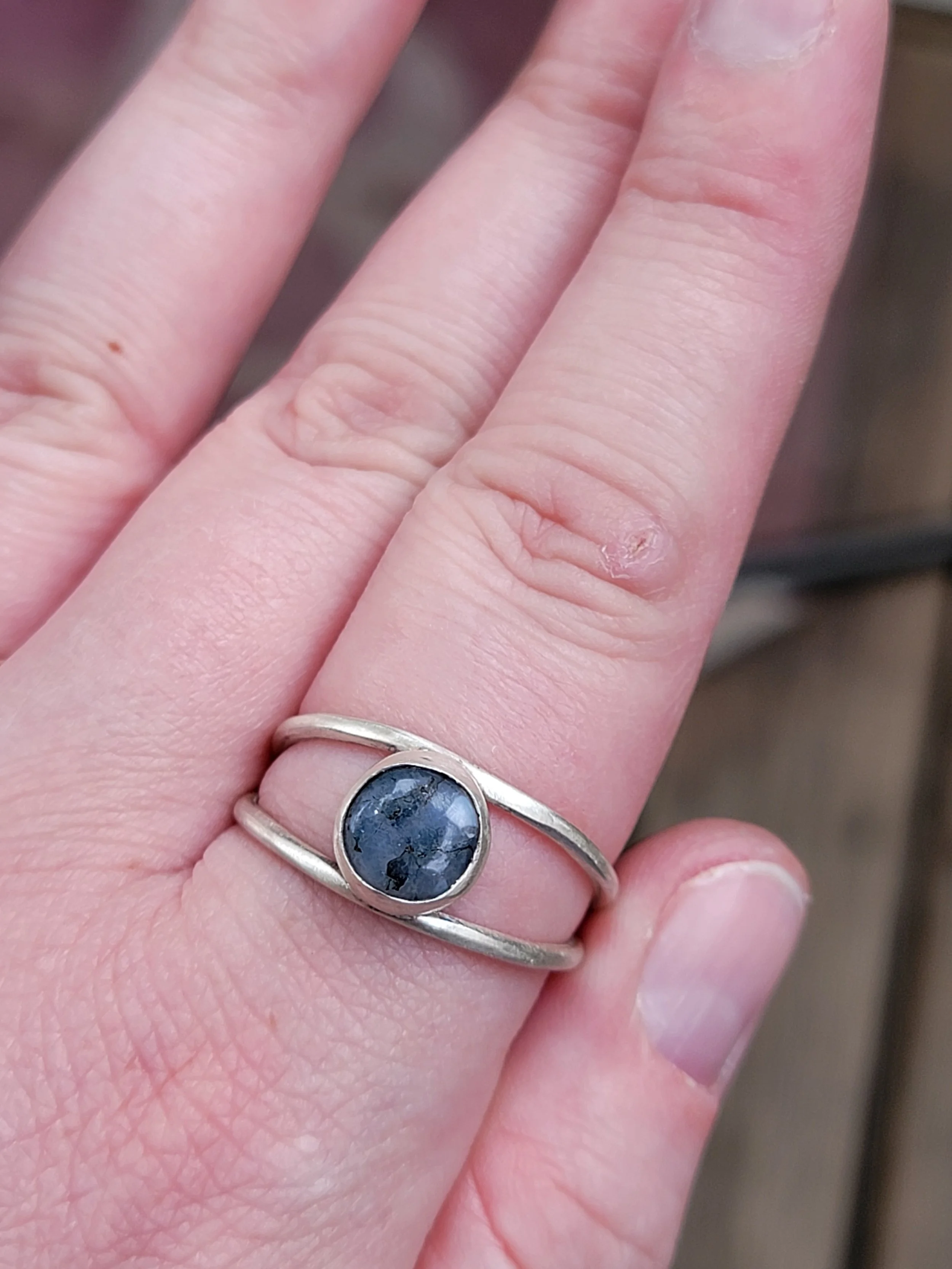 A hand with a silver ring featuring a dark, round stone on the finger.