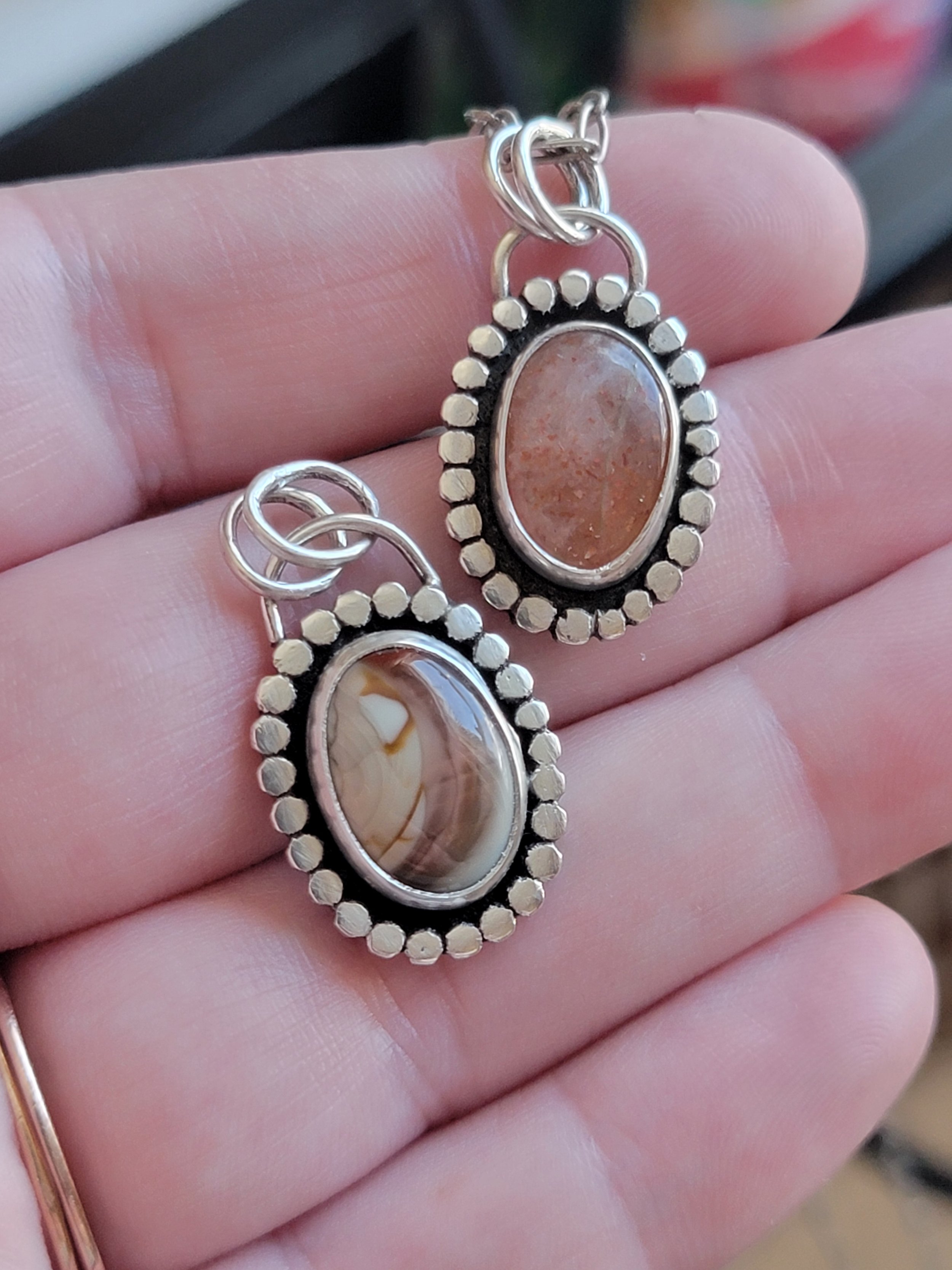 Silver earrings with oval cabochon stones, one with pinkish-brown mineral and the other with brown and white layered pattern, surrounded by small round silver beads.