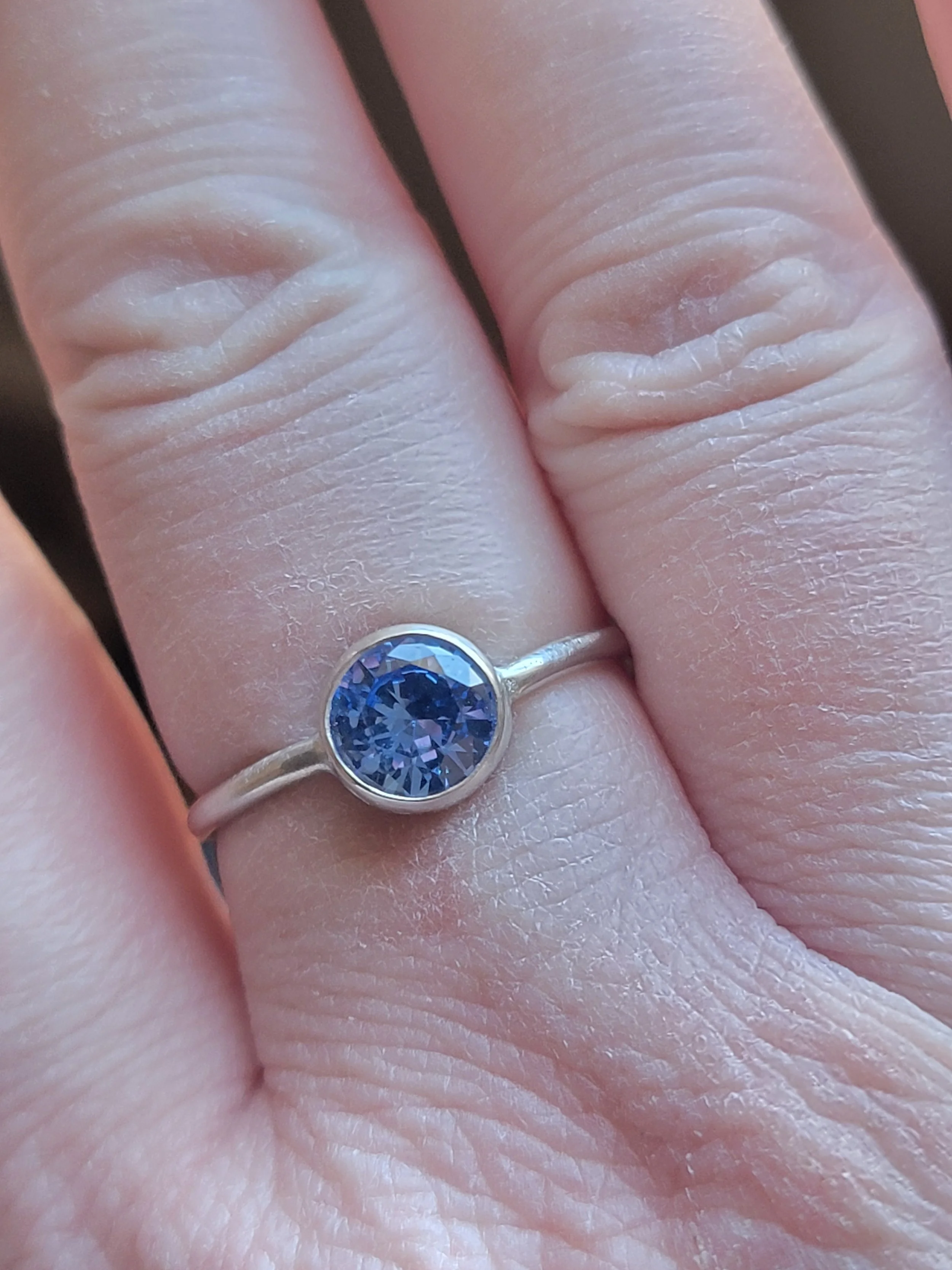 Close-up of a hand showing a ring with a large, round, blue gemstone on the ring finger.
