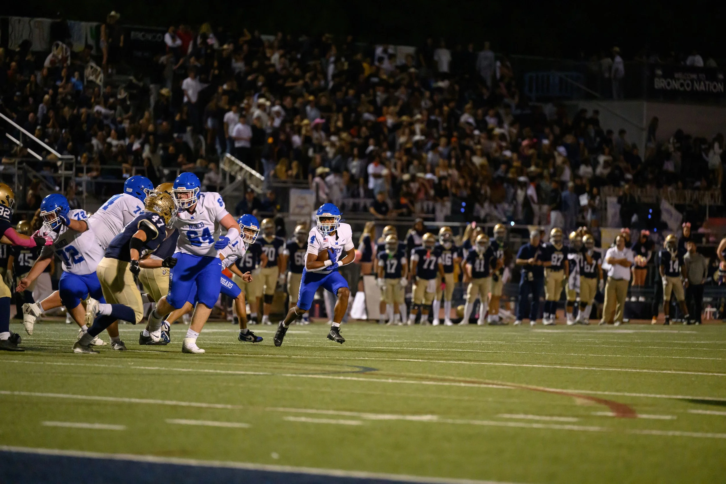 A football game in progress at night, with players on the field and spectators in the stands.